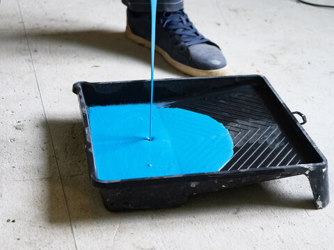 A jet of blue paint. The blue paint is poured into cuvette for rollers.