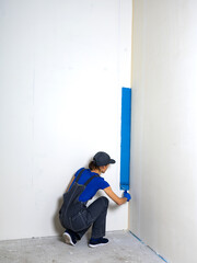 Female painter painting a white wall with a roller in blue color renovations or construction concept.