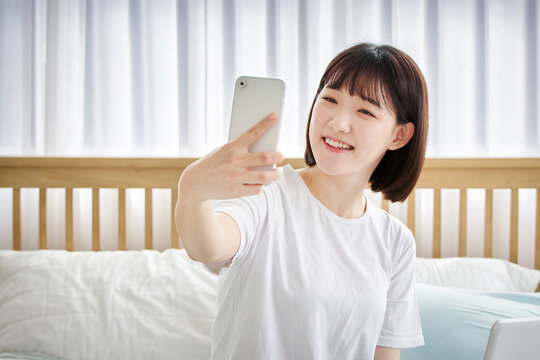 20대 젊은 한국여자가 침대에 앉아 있음. 통화, 사진촬영, 셀카, 사회관계망, 소통, 대화, 소셜미디어
