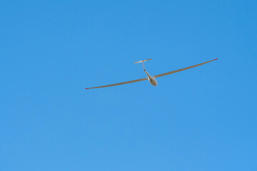 A Glider (sailplane) soaring on the background of blue sky on sunny day.