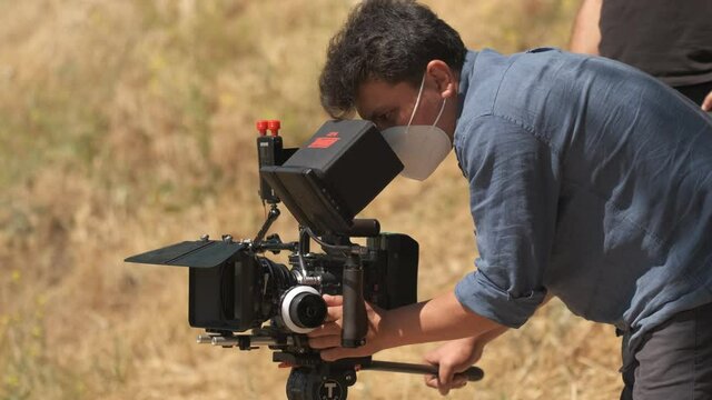Cameraman in denim shirt shoots on red camera in nature. Clouse-up on blurred background