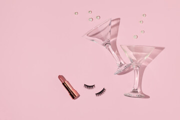 Creative layout with martini cocktail glasses, eyelashes, lipstick and white pearls on pastel pink...