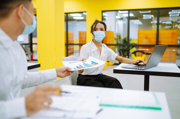 Office worker wearing medical face mask for social distancing  for virus prevention while using laptop back at work in office. Teamwork Process during pandemic in quarantine. Covid-19.