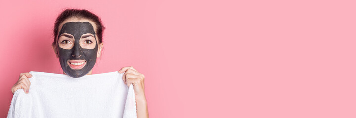 smiling nude girl covers herself with a towel with a face peeling mask on a pink background. Banner.