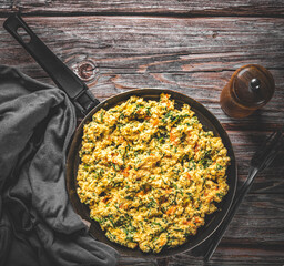 scrambled eggs with spinach and tomato in pan on wooden table background