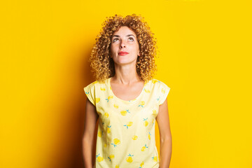 cute curly girl looks thoughtfully up on a yellow background.