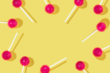 Creative pattern or frame made with bold pink lolly pops on bright yellow background. Sweet happy life inspiration. Cute colorful concept with lolly pop.