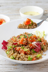 Healthy rustic quinoa salad with vegetables on a white wood table
