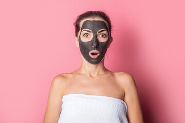 Surprised girl with bare shoulders, with a black clay mask on her face, spa treatments