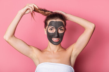 young woman smiling with clay mask on her face, ties her hair, home care