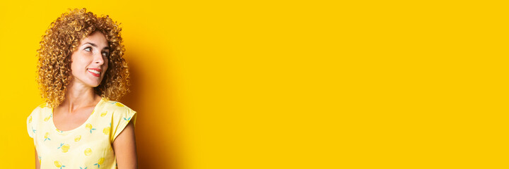 cute curly girl smiling looks to the side on a yellow background. Banner.