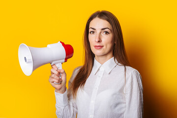 Young woman in a white shirt holds a megaphone in her hands on a yellow background. Hiring concept, help wanted. Banner