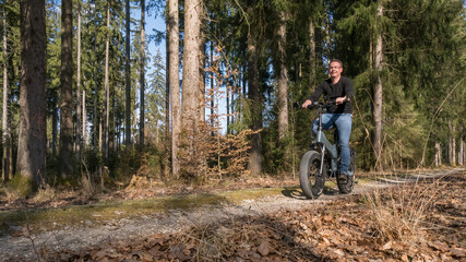 Young man rides big electric bike through the forest - 423393985