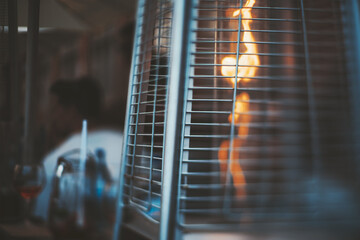 A true tilt-shift photo of a street gas heater for a patio with a flame of fire inside, with a...