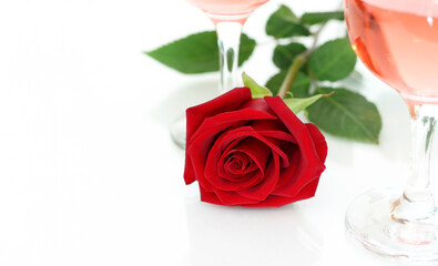 A red rose lies next to the wine glasses on a light background, there is a place for the text.