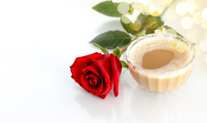 Coffee with milk in the morning light, next to a red rose.