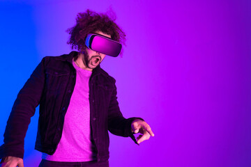 Surprised young man with afro hair touching the air and smiling during VR experience. Horizontal shot in studio. purple blue background