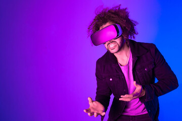 Surprised young man with afro hair touching the air and smiling during VR experience. Horizontal shot in studio. purple blue background