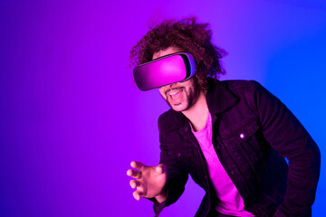 Surprised young man with afro hair touching the air and smiling during VR experience. Horizontal shot in studio. purple blue background