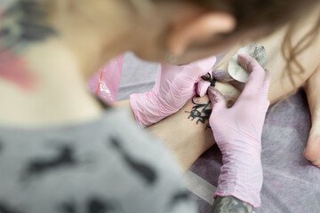 Close-up of a tattoo artist doing a tattoo on the leg of a young girl in the salon. Professional tattooist doing tattooing in studio
