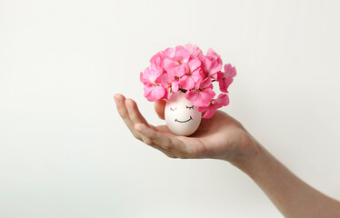 Hold the Easter egg in your hand. The egg is decorated with pink flowers and a face is drawn.