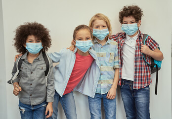 Cheerful diverse children wearing protective face masks looking at camera, posing together over light background