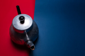 Close-up top view of vintage aluminum teapot on two backgrounds of red and blue colors.