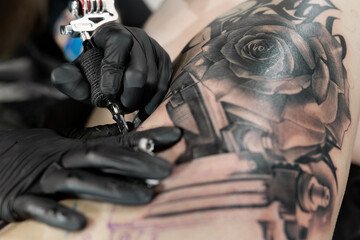 Fototapeta na wymiar Close up image of the bearded tattoo male artist makes a tattoo on a female leg