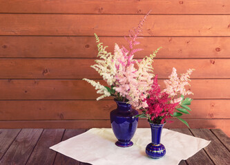 Red, white and pink beautiful astilbe flowers in blue vases on wooden table. Selective focus.
