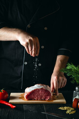 Chef sprinkles the meat with salt. Preparing meat before baking. Working environment in the kitchen of a restaurant or cafe