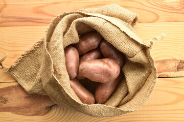 Several unpeeled raw potatoes in a jute bag on a wooden table, close-up, top view.