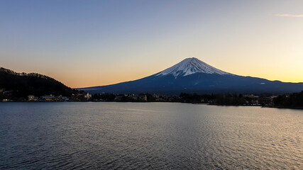 Idyllic view on Mt Fuji from the side of Kawaguchiko Lake, Japan. The mountain is surrounded by clouds. Calm surface of the lake moved by gentle wind. Serenity and calmness. Soft colors of the sunset