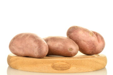 Three unpeeled raw potatoes on a round wooden tray, close-up, isolated on white.