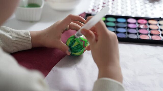 Close-up, children's hands are drawing a pattern on an Easter egg