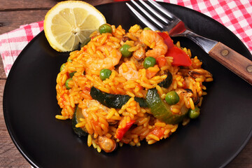 Gustoso piatto di paella catalana con fetta di limone e forchetta su sfondo rustico.