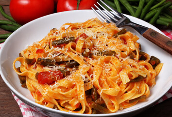 Piatto con gustose tagliatelle fatte in casa e condite con sugo di pomodoro e fagiolini verdi. Cibo vegetariano.