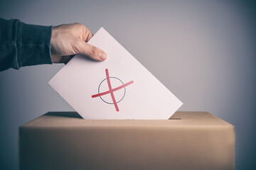 Wähler wirft Stimmzettel mit Kreuz in eine Wahlurne
