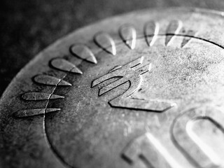 Translation of the inscription: rupee. Fragment of Indian 10 rupee coin with the sign of national currency close up. Dramatic dark black and white illustration about money and banking in India. Macro