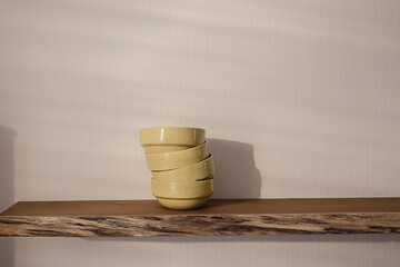 Open floating wooden shelf with a pile of four yellow handmade ceramic plates hanging on a white wallpaper wall in a modern design living room. Cozy minimalist home concept.