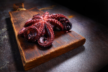Boiled whole octopus on a wooden cutting board. Cooking seafood dishes. Dark background. Protein food. Free place.