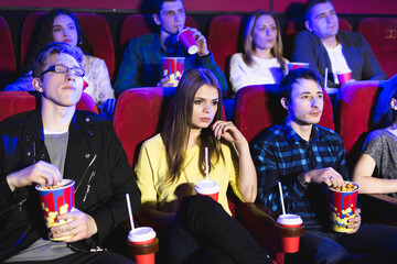 Friends sit and eat popcorn together while watching movies in a movie theater