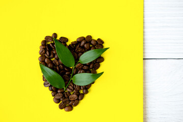 Coffee beans in the shape of a heart on a yellow background.