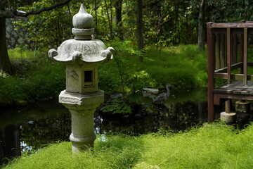 Fototapeta na wymiar Japanese traditional lantern near small river or canal in Japanese garden,egret bird on background with old terrace nearby in Japan.