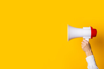 female hand holds a white with a red megaphone on a yellow background.