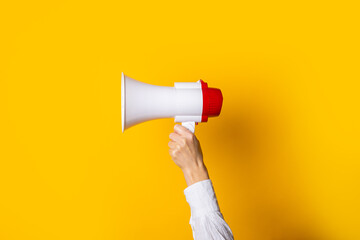 female hand holds a white with a red megaphone on a yellow background. - obrazy, fototapety, plakaty