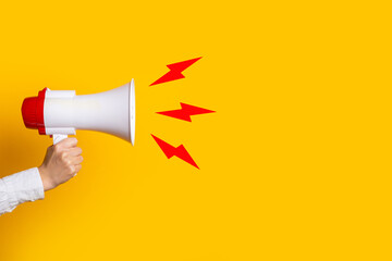 female hand holds a megaphone on a yellow background, added picture sound - obrazy, fototapety, plakaty