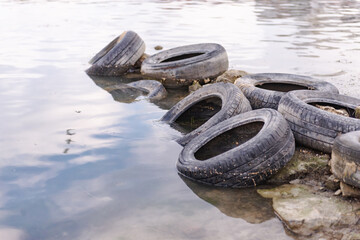 Old tires on the beach. Pollution of the reservoir with old car tires. Garbage on the shore