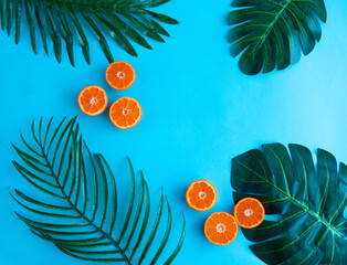 Composition from palm leaves, monstera and tangerine on a blue background. Summer concept. View from above. Copy space
