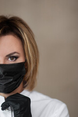 Close-up portrait of beautician in black medical gloves and black medical mask