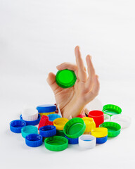 A woman's hand is covered with plastic bottle caps. The girl shows the "ok" gesture and holds a plastic stopper for recycling and recycling